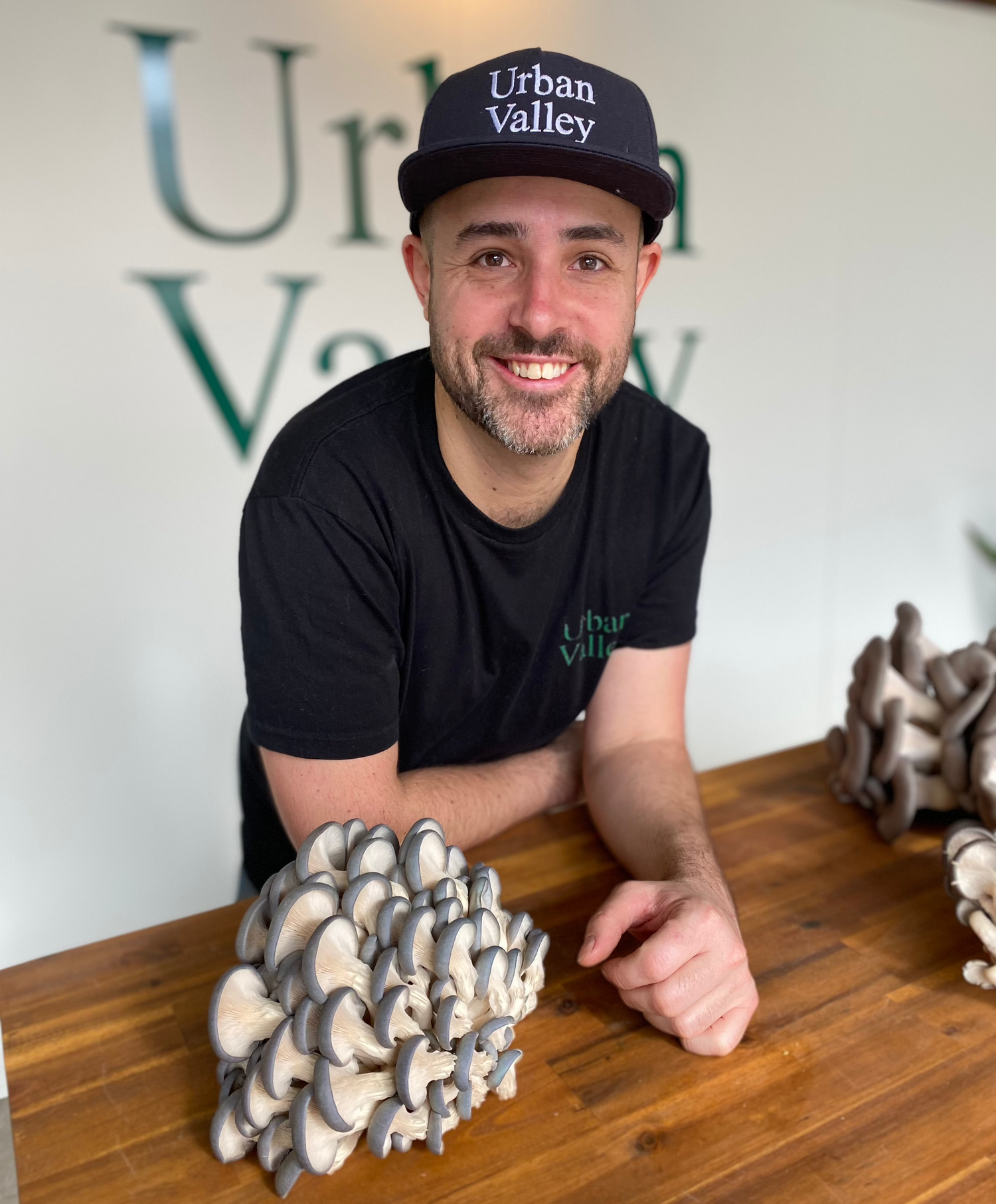 A handsome portrait of Joel from Urban Valley mushroom farm in Brisbane at his farm with clusters of harvested oyster mushrooms